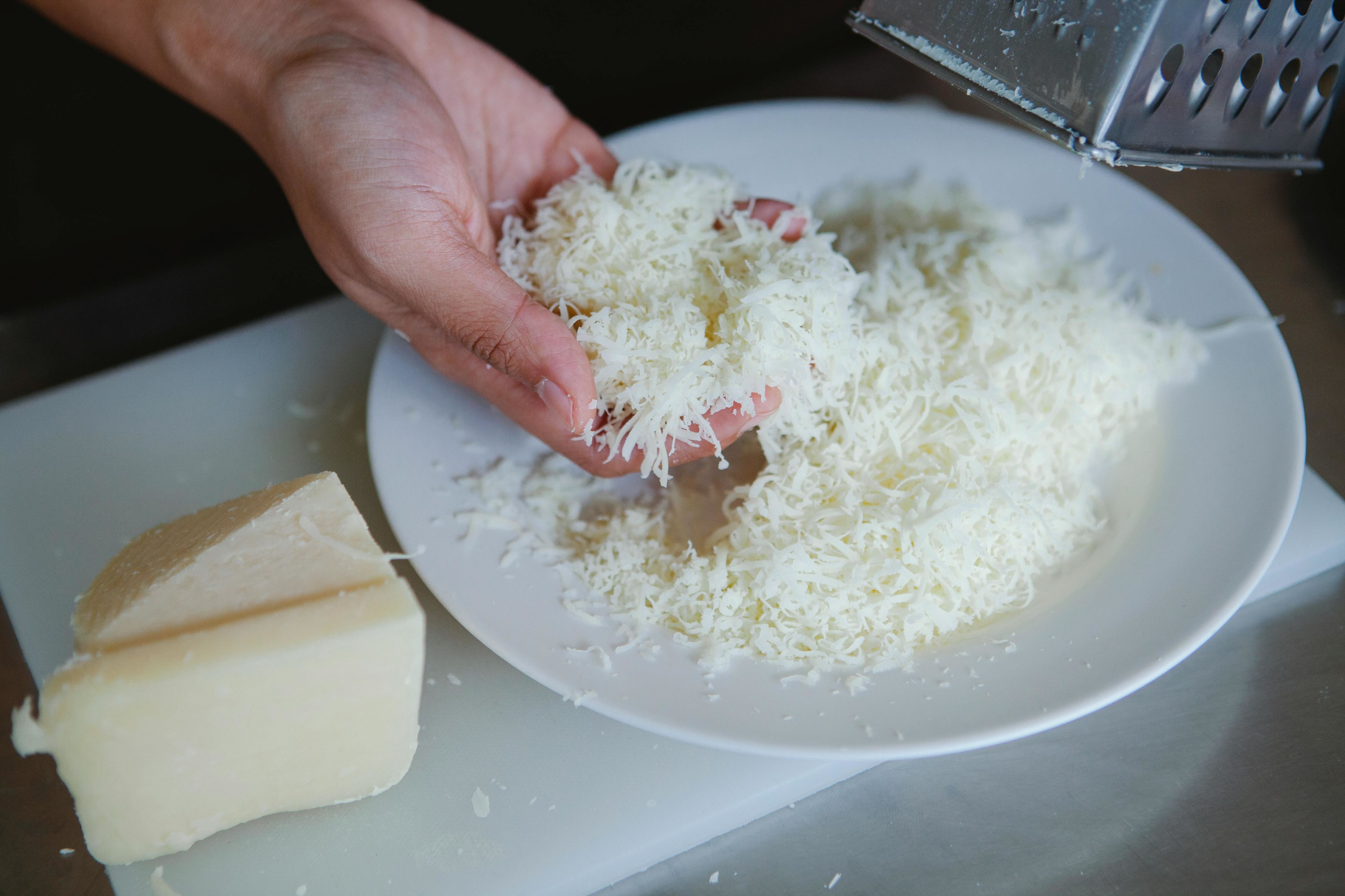 Hand grating cheese onto a plate, showcasing fresh dairy product.